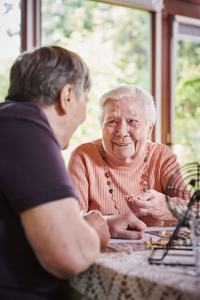 Eine alte und eine jüngere Person sitzen an einem Tisch und unterhalten sich.