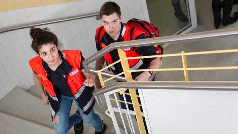 Malteser Schulsanitäter in Einsatzkleidung gehen eine Treppe hoch.