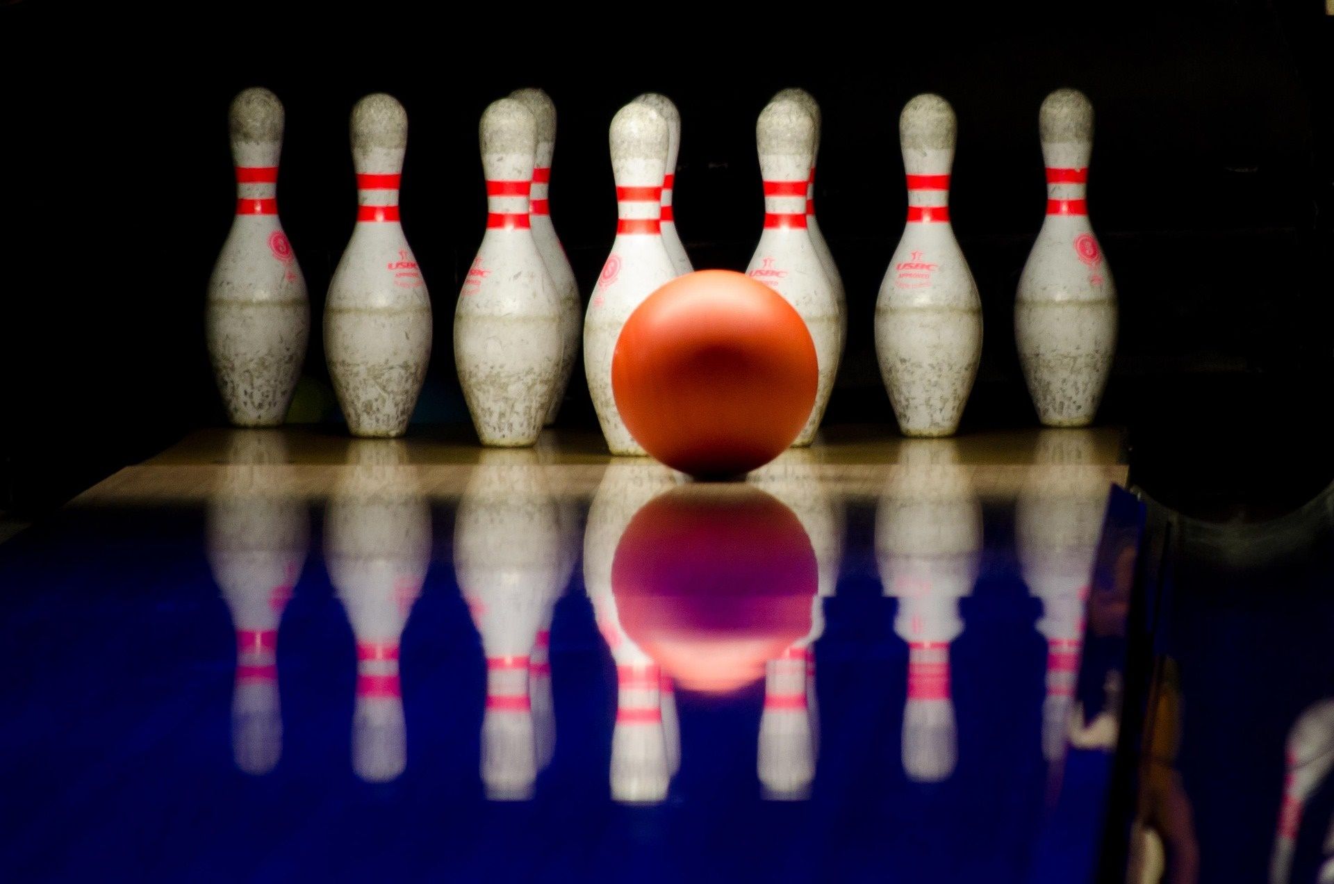 Neun Kegel in Weiß mit rotem Rand, davor eine rote Bowlingkugel