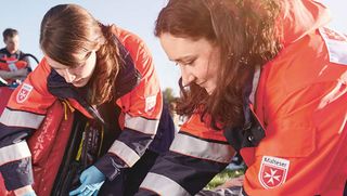 Malteser Sanitäterinnen versorgen einen Verletzten, der auf einer Wiese liegt.