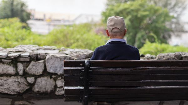 Älterer Mann sitzt mit dem Rücken zur Kamera auf einer Parkbank.