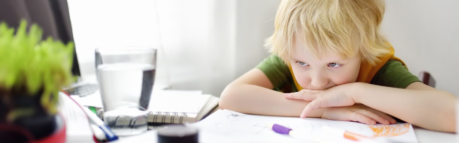 Ein kleiner Junge sitzt mit unglücklichem Gesichtsausdruck an einem Tisch.