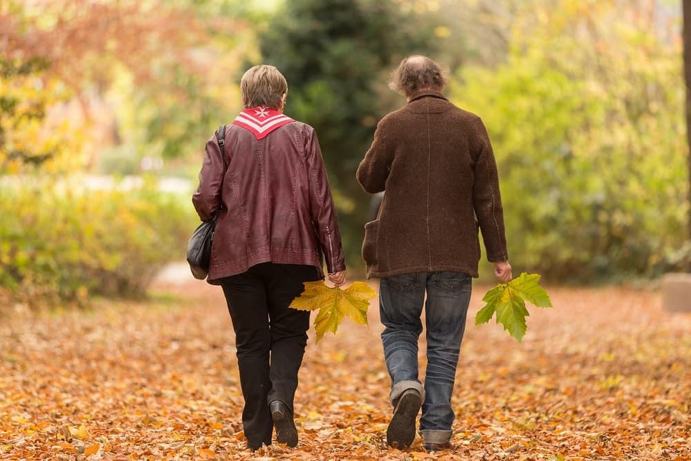 Malteser Mitarbeiterin geht mit Mann im herbstlichen Park spazieren