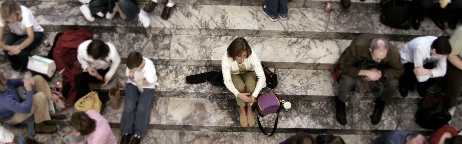 Gruppe von Menschen sitzen auf einer Treppe, eine Person sitzt isoliert