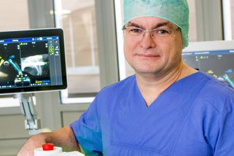 Mann in OP-Kleidung und Haube hält einen Roboterarm in einem Behandlungsraum.