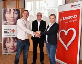 Drei Personen stehen zusammen vor einem historischen Bild.