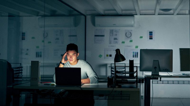 Junger asiatischer Mann in einem dunklen Büro vor einem Bildschirm