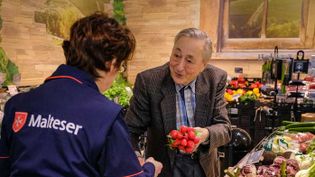 Malteser Helferin unterstützt einen älteren Mann beim Einkaufen im Supermarkt.