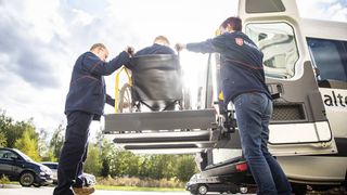 Zwei Mitarbeitende des Malteser Fahrdienstes helfen einer Person im Rollstuhl.