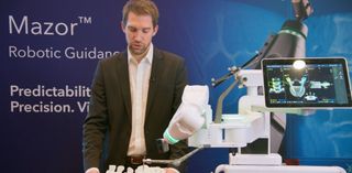 Person präsentiert den Wirbelsäulenroboter Mazor X mit Modellwirbelsäule und Bildschir-mansicht.