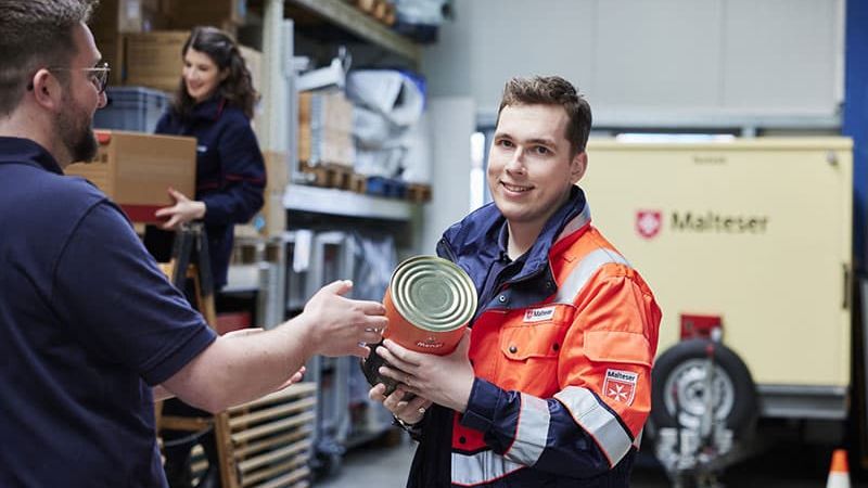 Mann in Malteser Einsatzkleidung packt Konserven ein. 