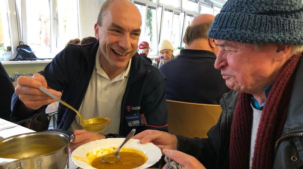 Ein Malteser Helfer füllt einem Obdachlosen Suppe auf den Teller.