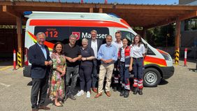 Mehrere Menschen stehen nebeneinander vor einem Malteser Rettungswagen