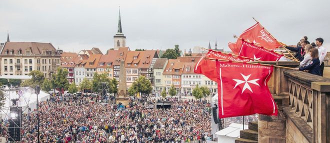 Menschenmenge und Bannerträger der Malteser vor einem Dom