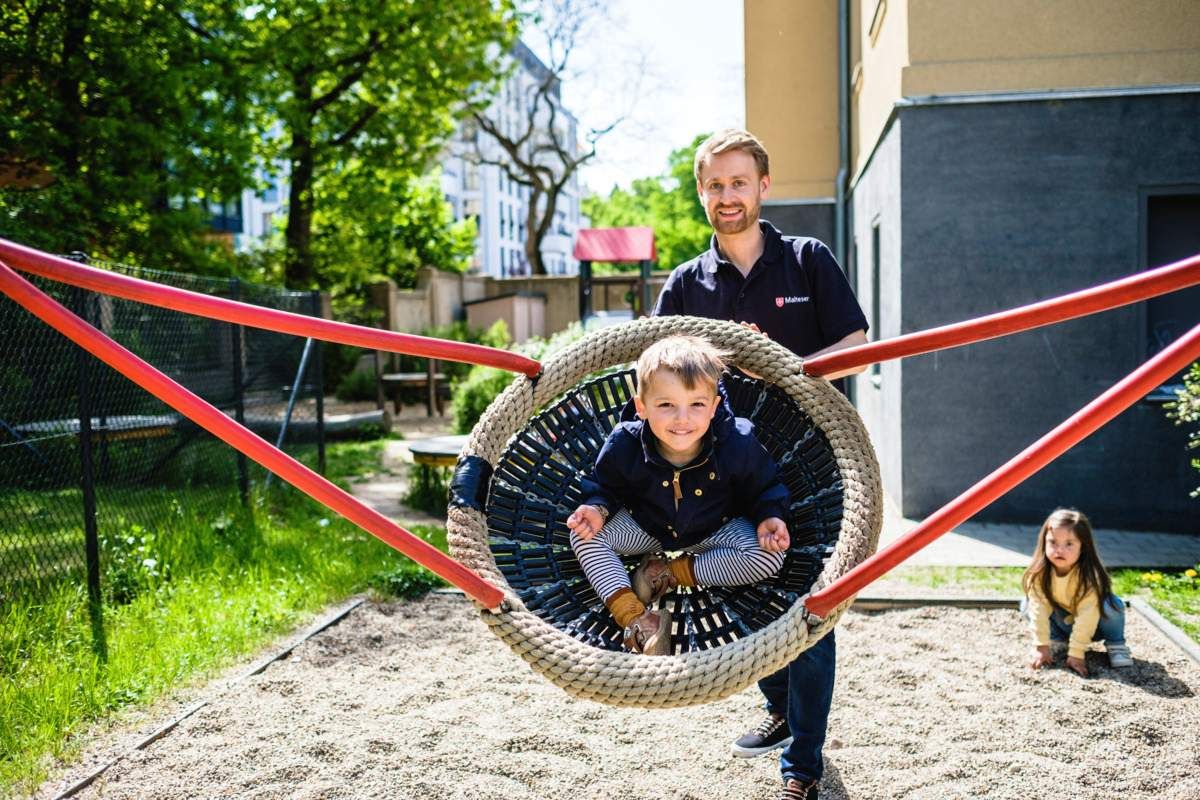 Ein Kind in einer Korbschaukel auf einem Spielplatz mit einem jungen Mann 