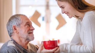 Eine Frau reicht einem älteren Mann eine rote Tasse.