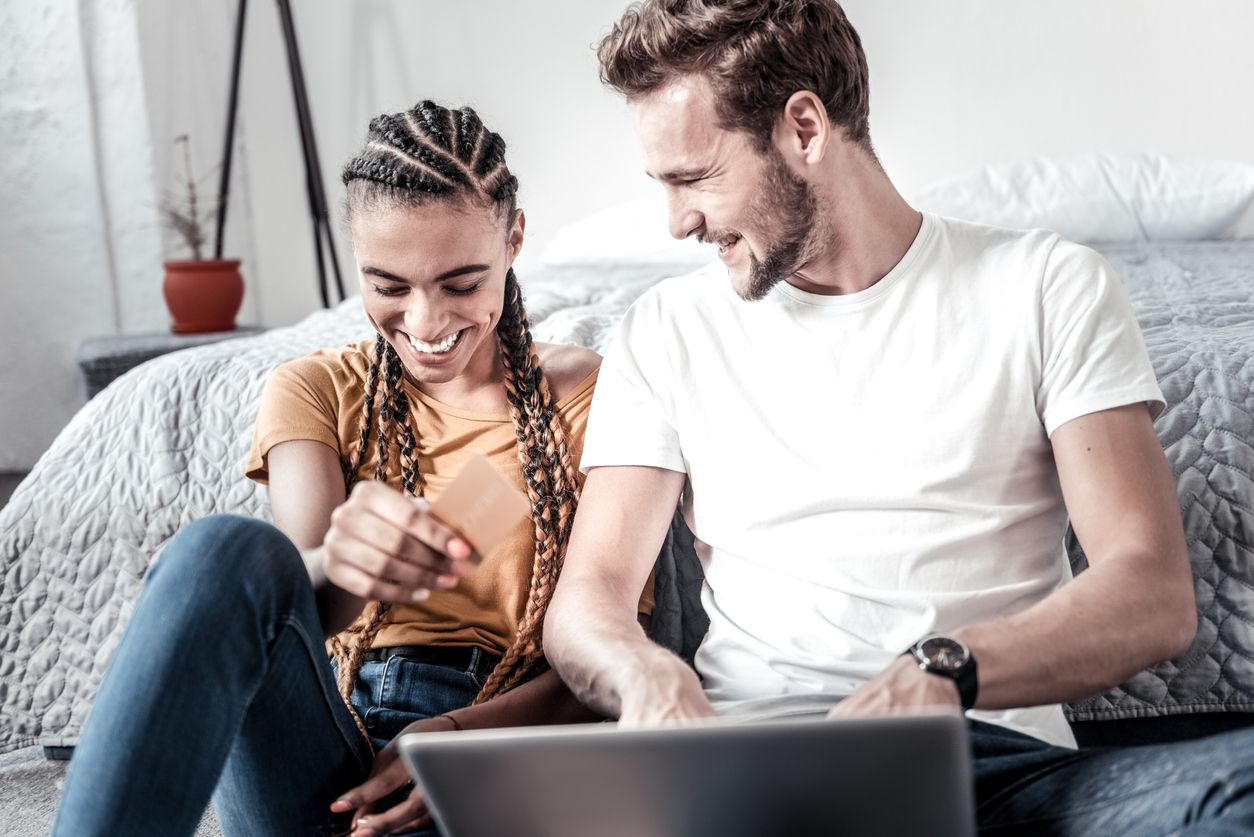Junge Frau und junger Mann lachend auf einem Sofa mit Laptop