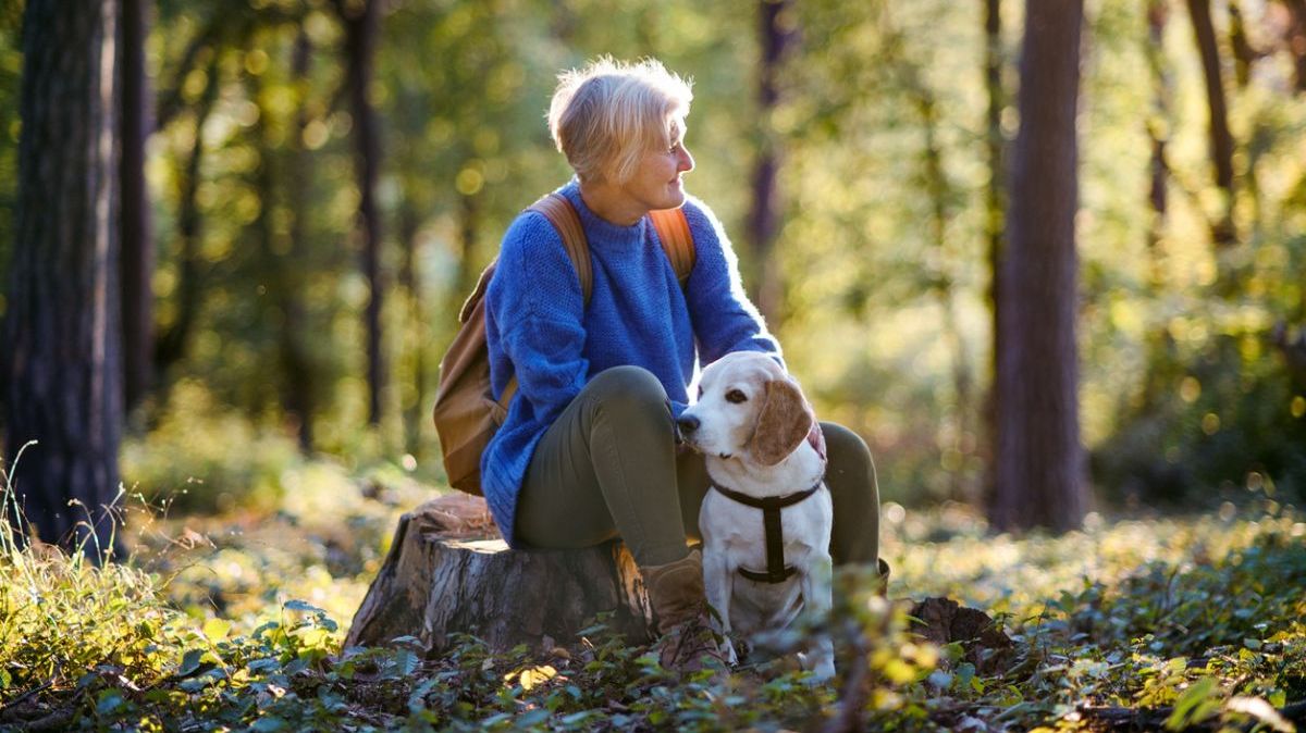 Eine ältere Frau mit Hund in einem Wald.