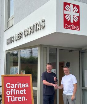 zwei Männer stehen vor dem Eingang der Caritas in Cottbus. Sie schütteln sich die Hände.