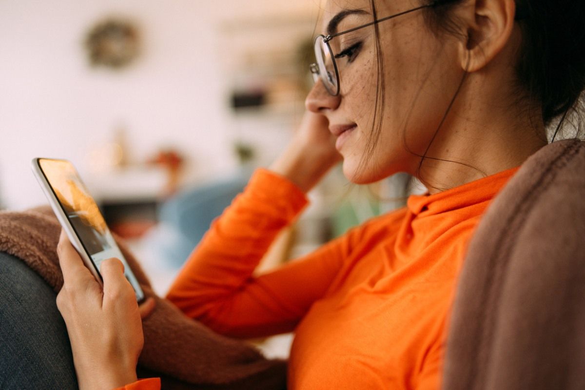 Junge Frau mit Brille schaut auf ein Smartphone.