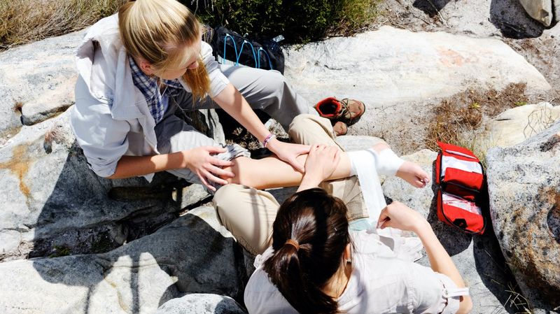 Eine Frau verbindet den Fuß einer anderen Frau, die auf Felsen sitzt.