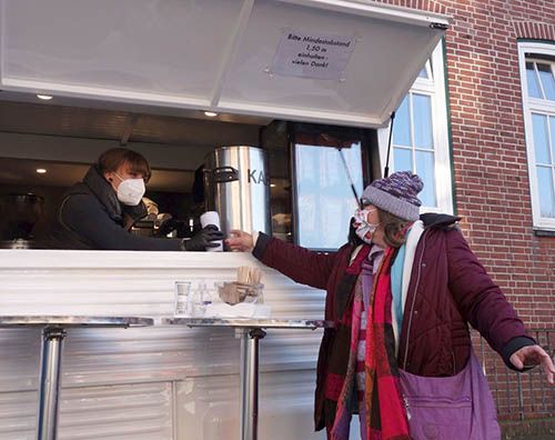 Frau in einem Wagen reicht einer anderen Frau einen Bescher Kaffee