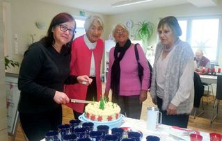 Vier Frauen stehen um eine weihnachtlich dekorierte Torte, eine schneidet sie gerade mit einem Messer an.