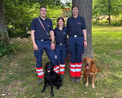 Abgebildet sind drei Personen in Einsatzbekleiung des Malteser Hilfsdienst sowie zwei Hunde, die die Prüfung als Kadaverspürhunde erfolgreich abgelegt haben.