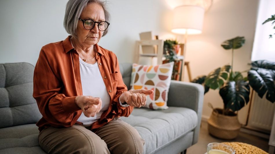 Eine ältere Frau sitzt auf einem Sofa und schaut ernst auf ihre zu Fäusten geschlossenen Hände