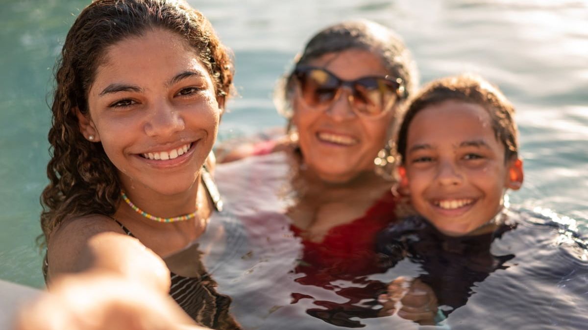 Ältere lächelnde Frau mit Sonnenbrille mit zwei Kindern bis zum Hals im Wasser.