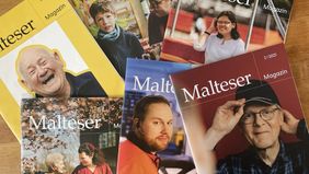 Sechs Ausgaben des „Malteser Magazin“ liegen überlappend auf Holz, mit verschiedenfarbigen Covern und teils unscharfen Personenfotos.