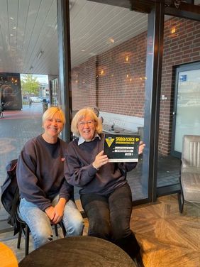 Zwei Ehrenamtliche im Café beim E-Center Bruns mit dem symbolischen Scheck