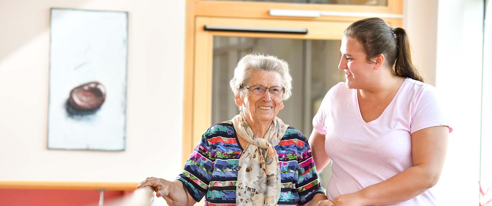 Pflegerin begleitet Bewohnerin durch den Flur 