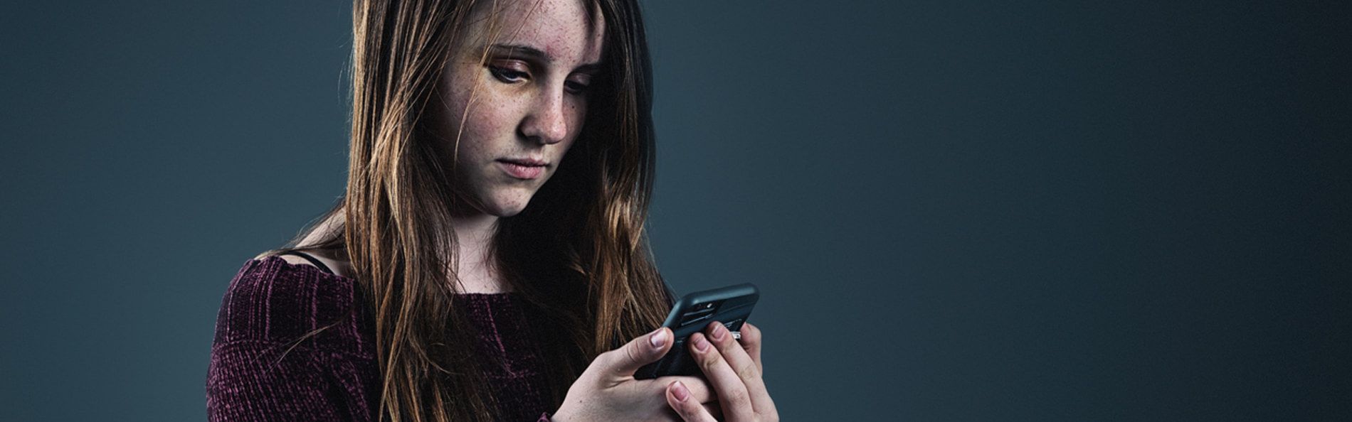 Junges Mädchen schaut mit resigniertem Gesichtsausdruck auf ein Smartphone
