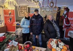 Drei Personen in Winterjacken stehen hinter einem Tisch mit Weihnachtsartikeln