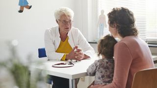 Eine Frau mit ihrem Kind spricht mit einer Ärztin in einer Praxis.