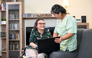 Zwei Frauen sitzen lachend auf dem Sofa und schauen gemeinsam auf einen Laptop drauf