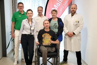 Patient im Rollstuhl mit sechs medizinischen Fachkräften in Klinikflur.