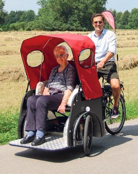 Eine Frau sitzt in einer Fahrradrikscha, hinter ihr sitzt ein Mann, der die Rikscha fährt.