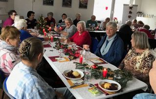 Seniorinnen und Senioren an einem gedeckten Tisch mit Essen 