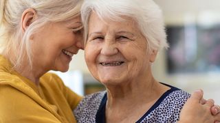 Frau umarmt ihr alte Mutter. Beide lachen. 