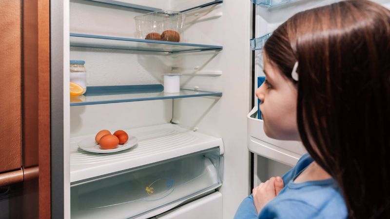 Ein kleines Mädchen schaut in einen fast leeren Kühlschrank.