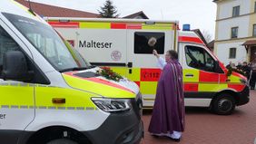 Ein Mann in liturgischer Kleidung segnet zwei Einsatzfahrzeuge draußen.