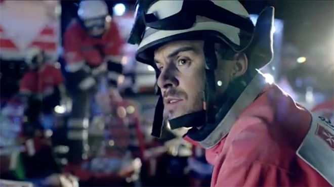 Vorschaubild für das Video bei youtube: Im Vordergrund ein ehrenamtlicher Katastrophenschutz-Helfer der Malteser in Nahaufnahme, im Hintergrund das Szenario einer Katastrophenschutzübung bei Dunkelheit