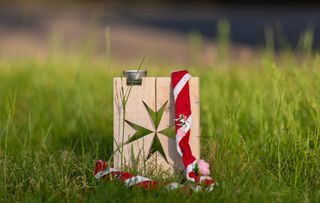 Malteser Kreuz aus Holz steht in der Wiese und auf ihm liegt ein Malteser Jugend Tuch