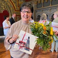 Eine Frau hält eine Urkunde und Blumen.