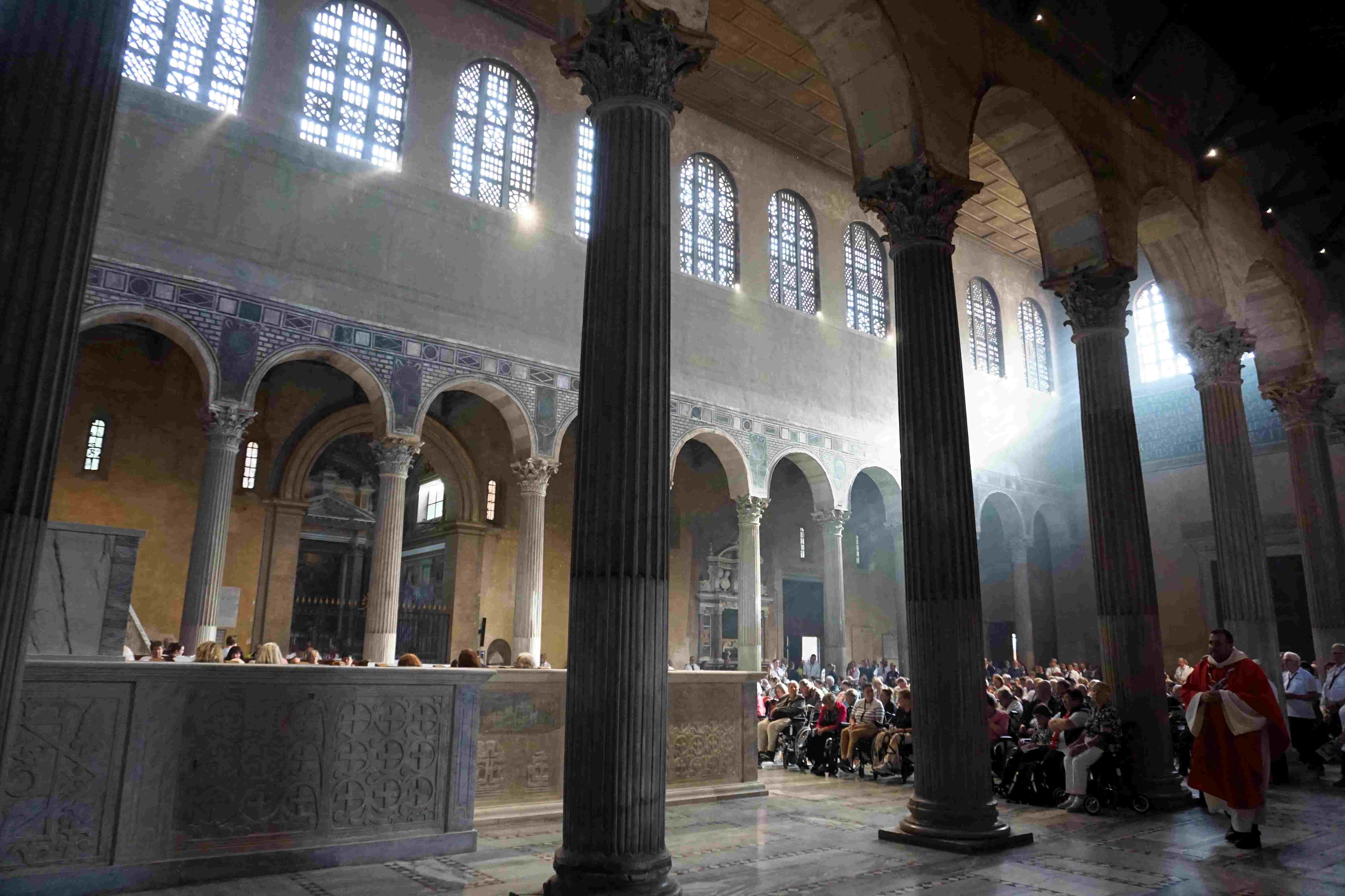 Innenraum einer Kirche mit hohen Säulen und Lichtstrahlen, die durch Fenster fallen.