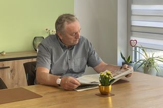 Ein Senior mit einem Hausnotruf-Armband beim Zeitunglesen