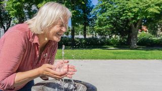 Seniorin macht ihr Gesicht an einem Brunnen nass, um der Hitze entgegenzuwirken.