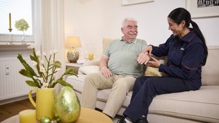 Eine Hausnotruf Mitarbeiterin legt einem Senioren ein Hausnotrufarmband an